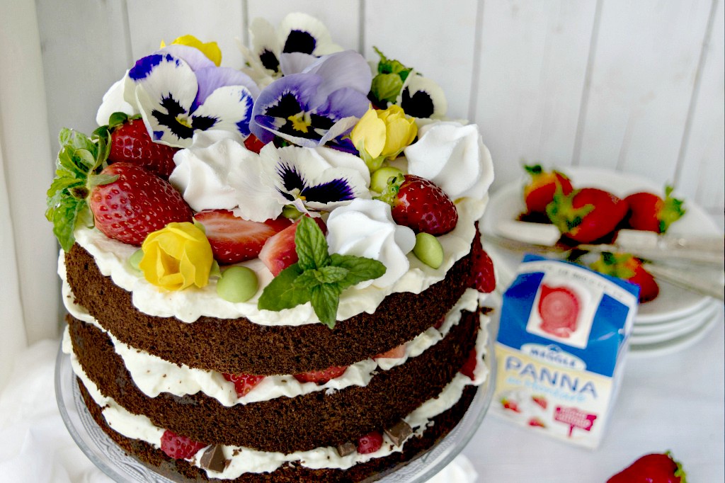 Chiffon cake al cioccolato con panna e fragole con fiori e meringhe